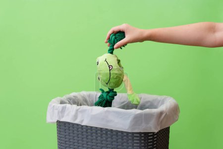 Photo for Woman putting a broken toy in waste bin on a green background, copy space - Royalty Free Image
