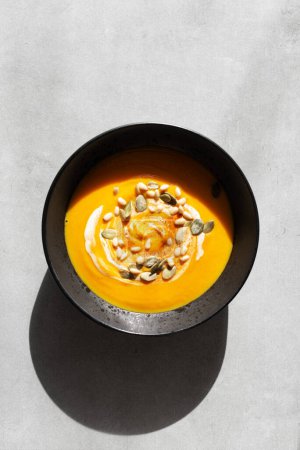 Photo for Seasonal autumn food. Pumpkin soup with cream, croutons and pumpkin seeds in a black plate on a gray background. Top view, copy space, minimalist - Royalty Free Image