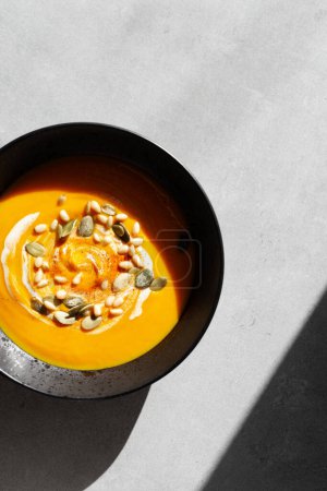 Photo for Seasonal autumn food. Pumpkin soup with cream, croutons and pumpkin seeds in a black plate on a gray background. Top view, copy space, minimalist - Royalty Free Image
