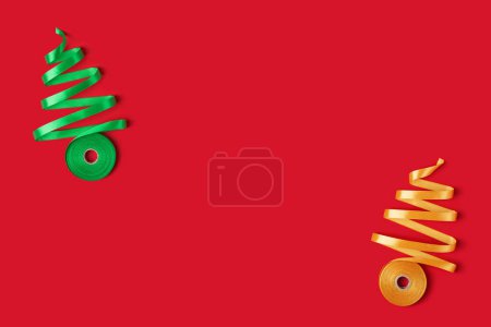 Téléchargez les photos : Carte du Nouvel An avec concept d'arbres de Noël en ruban doré et vert sur fond rouge. Vue du dessus, espace de copie - en image libre de droit