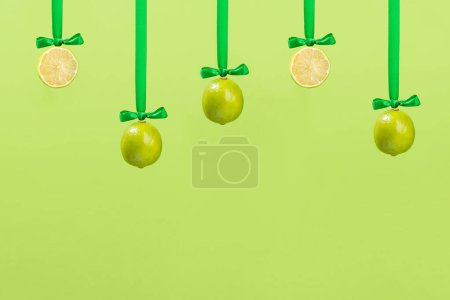 Téléchargez les photos : Boule de Noël décoration de citron vert avec ruban de satin et arc sur fond vert. Nouvelle année concept créatif, espace de copie - en image libre de droit
