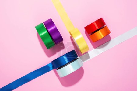 Téléchargez les photos : Ensemble de bobines de ruban de satin coloré sur fond rose. Ruban textile pourpre, jaune, vert, bleu, rouge et orange, vue de dessus - en image libre de droit