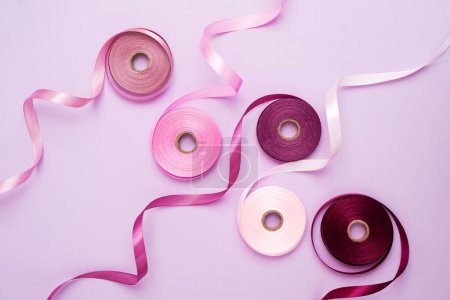 Foto de Conjunto de coloridos carretes de cinta de satén sobre fondo púrpura claro. Carretes de cinta textil púrpura y rosa, vista superior - Imagen libre de derechos