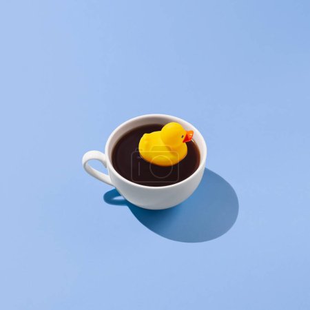 Téléchargez les photos : Tasse à café avec un canard en caoutchouc jaune sur fond bleu, concept de boisson créatif - en image libre de droit