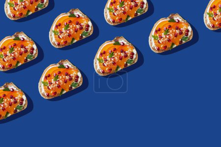 Photo for Pattern of toasts with cream cheese, persimmon and pomegranate seeds on blue background. Creative food photo concept. Top view, copy space - Royalty Free Image