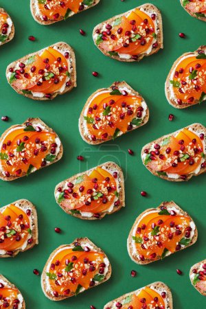 Foto de Patrón de tostadas con queso crema, caqui y semillas de granada sobre fondo verde. Concepto de foto de comida creativa, vista superior - Imagen libre de derechos