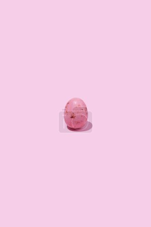 One pink shiny Easter egg casting shadow on pink background, minimalism concept, copy space