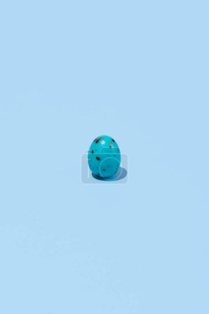One blue shiny Easter egg casting shadow on blue background, minimalism concept, copy space