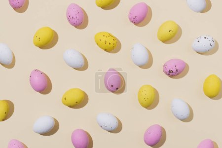 Téléchargez les photos : Modèle d'oeufs de Pâques en chocolat de couleur blanche, rose et jaune sur un fond beige. Concept créatif de Pâques, vue de dessus - en image libre de droit