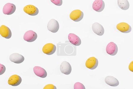 Téléchargez les photos : Modèle d'oeufs de Pâques en chocolat de couleur blanche, rose et jaune sur un fond blanc. Concept créatif de Pâques, vue de dessus - en image libre de droit