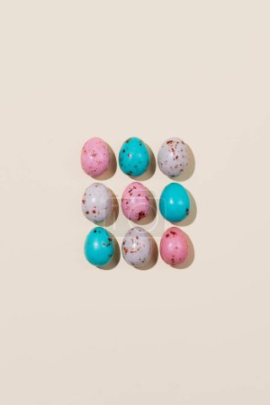 Foto de Patrón de huevos de Pascua de chocolate en colores rosa, beige y azul sobre un fondo beige. Concepto creativo de Pascua, vista superior - Imagen libre de derechos