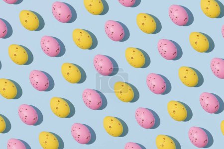 Photo for Pattern of chocolate Easter eggs in pink and yellow colors on a blue background. Creative Easter concept, top view - Royalty Free Image