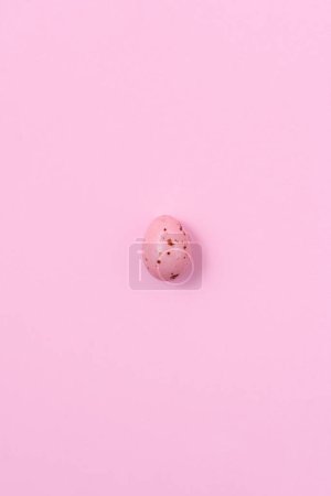 Téléchargez les photos : Un œuf de Pâques rose moucheté projetant une ombre sur un fond rose. Concept de minimalisme, espace de copie, vue de dessus - en image libre de droit