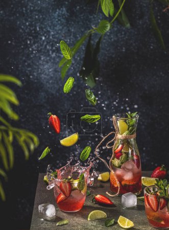 Cocktail with lime, crushed ice, strawberries and mint with fly ingredients on the dark background, selective focus image, copy spice for you text, summer vacation and party concept.