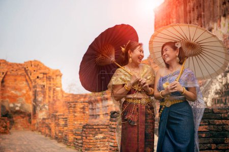 Téléchargez les photos : Visage de bonheur de deux femmes asiatiques portant vieux costume traditionnel thaï avec parapluie en bambou debout dans le vieux temple à ayutthaya site du patrimoine mondial de thaïlande de l'Unesco - en image libre de droit