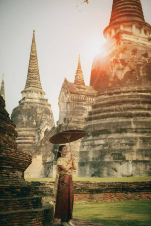 Téléchargez les photos : Femme asiatique tenant parapluie en bambou debout contre stupa dans l'ancien temple de ayutthaya site du patrimoine mondial de l'Unesco central de Thaïlande - en image libre de droit