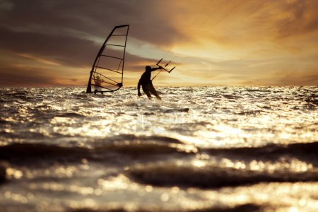 Téléchargez les photos : Silhouette photographie de l'homme jouant kite surf et planche à voile sur le niveau de la mer se précipitant contre le beau ciel couchant - en image libre de droit