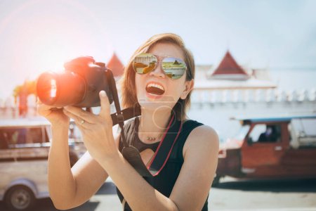 Téléchargez les photos : Visage de bonheur de la femme asiatique tenant caméra dslr debout dans la vieille ville de ayutthaya site du patrimoine mondial de l'Unesco Thaïlande - en image libre de droit
