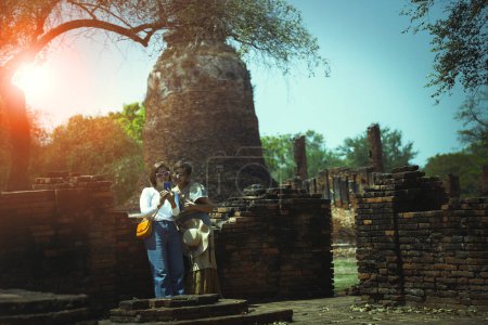 Téléchargez les photos : Couples de femmes asiatiques debout dans le vieux temple de ayutthaya et regardant sur l'écran de téléphone intelligent, ayuttha est l'une des destinations de voyage les plus populaires en Thaïlande - en image libre de droit