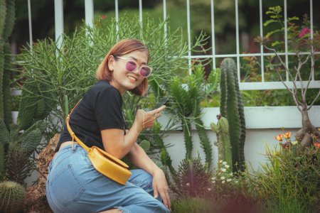 Téléchargez les photos : Asiatique femme tenant smartphone dans la main dents sourire visage avec bonheur dans belle maison jardin - en image libre de droit