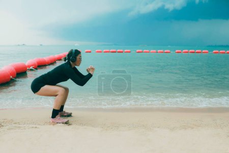 Téléchargez les photos : Femme portant casque approchant pour l'exercice squat à la plage de la mer - en image libre de droit
