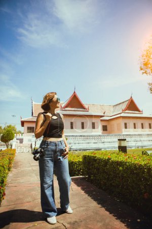 Téléchargez les photos : Femme tenant dslr caméra debout en plein air avec thai style de construction de la culture - en image libre de droit