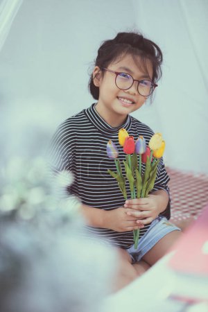 Téléchargez les photos : Asiatique enfant tenant artificielle de tulipe fleur dans la main dents sourire avec bonheur - en image libre de droit