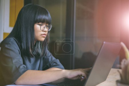 Téléchargez les photos : Asiatique adolescent assis dans salle de travail et lecture message sur ordinateur portable écran - en image libre de droit