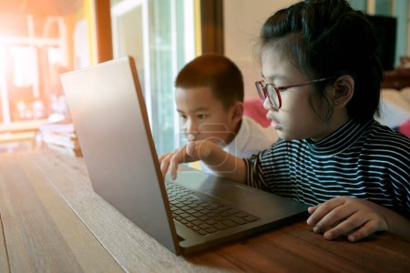 Téléchargez les photos : Deux asiatiques enfants apprendre à utiliser ordinateur portable à la maison salon - en image libre de droit