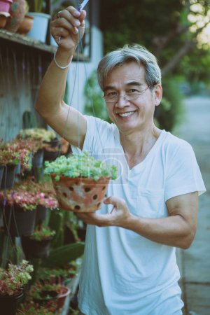 Téléchargez les photos : Asiatique tenant pendaison plante d'intérieur pot dents souriant avec bonheur visage debout extérieur - en image libre de droit