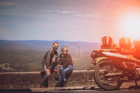 Téléchargez les photos : Couples de motard toothy sourire avec bonheur à côté de la petite moto à destination de voyage - en image libre de droit