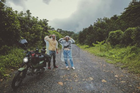 Téléchargez les photos : Couples de motards asiatiques portant des vêtements de pluie en plastique debout à côté de la petite moto enduro sur la piste de pays - en image libre de droit