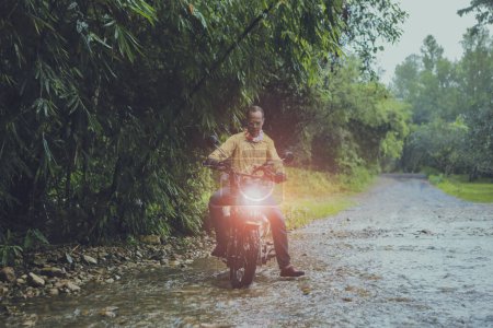Téléchargez les photos : Asiatique homme équitation petit enduro moto traversant coulant ruisseau dans forêt parmi la pluie tomber - en image libre de droit