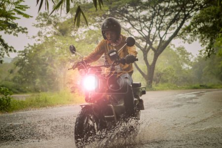 Téléchargez les photos : Homme chevauchant petite moto endurom traversant ruisseau peu profond parmi la pluie tombant à la forêt - en image libre de droit