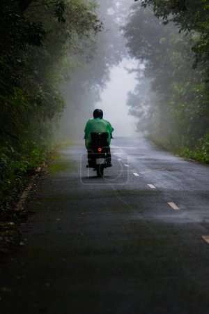 Téléchargez les photos : Cycliste portant un imperméable en plastique chevauchant sur la route de montagne brumeuse au parc national de Khao Yai Thaïlande - en image libre de droit