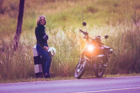Téléchargez les photos : Jolie femme tenant casque de sécurité debout sur la route locale à côté de la petite moto enduro - en image libre de droit