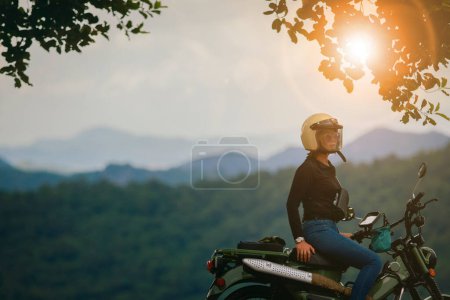 Téléchargez les photos : Femme portant un casque de sécurité assis sur une petite moto enduro contre de beaux paysages de Thaïlande parc national khao yai - en image libre de droit