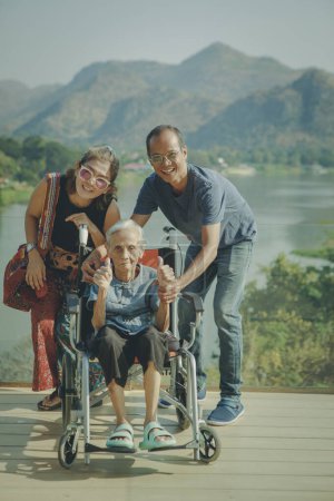 Téléchargez les photos : Heureux asiatique famille avec grand-mère assis sur fauteuil roulant - en image libre de droit
