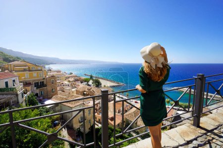 Téléchargez les photos : Vacances en Italie. Femme touristique avec chapeau de paille bénéficiant d'une vue sur le village de Pizzo depuis la terrasse en Calabre, Italie. - en image libre de droit
