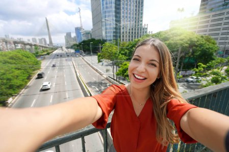 Foto de Turismo en Sao Paulo. Hermosa chica sonriente toma autorretrato con Ponte Estaiada puente en Sao Paulo metrópoli, Brasil. - Imagen libre de derechos