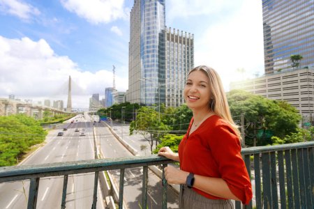 Foto de Viajar a Sao Paulo, Brasil. Retrato de una hermosa chica sonriente con paisaje urbano de Sao Paulo y puente Ponte Estaiada en el fondo, Sao Paulo, Brasil. - Imagen libre de derechos