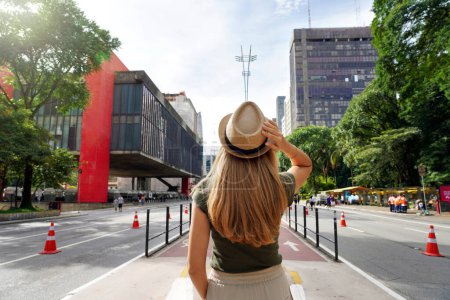 Photo for Visiting Sao Paulo City, Brazil. Rear view of beautiful tourist woman with hat walking along Paulista Avenue, Sao Paulo, Brazil. - Royalty Free Image