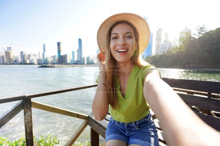 Photo for Happy smiling stylish female model takes self portrait with her smartphone in Balneario Camboriu, Santa Catarina, Brazil - Royalty Free Image