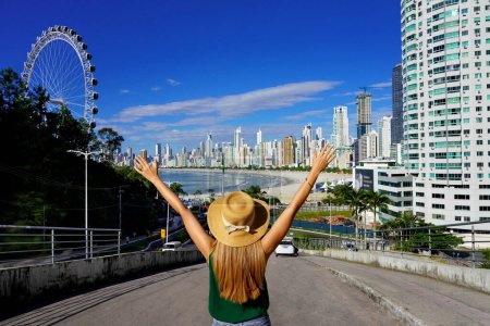 Photo for Girl with raised arms on Balneario Camboriu skyline with Ferris Wheel, Santa Catarina, Brazil - Royalty Free Image