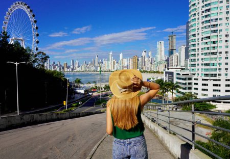 Photo for Holidays in Brazil. Rear view of young woman with hat enjoying Balneario Camboriu city skyline, Santa Catarina, Brazil. - Royalty Free Image
