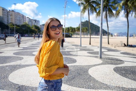 Portrait of attractive smiling woman walking along Copacabana beach promenade and turns to the camera, Rio de Janeiro, Brazil