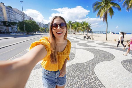 Téléchargez les photos : Femme touriste de mode prend selfie photo sur Copacabana plage promenade, Rio de Janeiro, Brésil - en image libre de droit