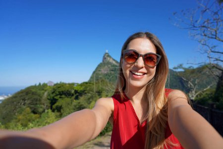 Brazilian tourist woman takes selfie on Mirante Dona Marta viewpoint with Corcovado mountain on the background, Rio de Janeiro, Brazil.