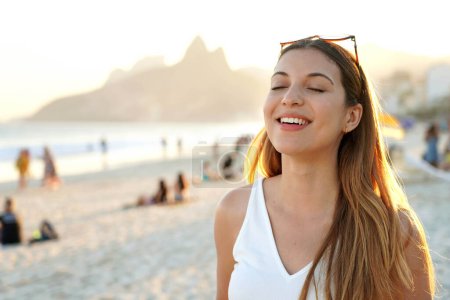 Portrait of young smiling Brazilian woman with closed eyes on Ipanema beach at sunset in Rio de Janeiro, Brazil