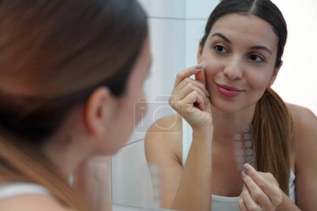 Photo for Close-up of pretty woman applying acne treatment anti-pickel patch on a pimple on her face at home - Royalty Free Image